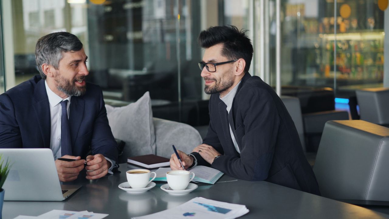 Two businessmen having a discussion over coffee in a modern office setting.