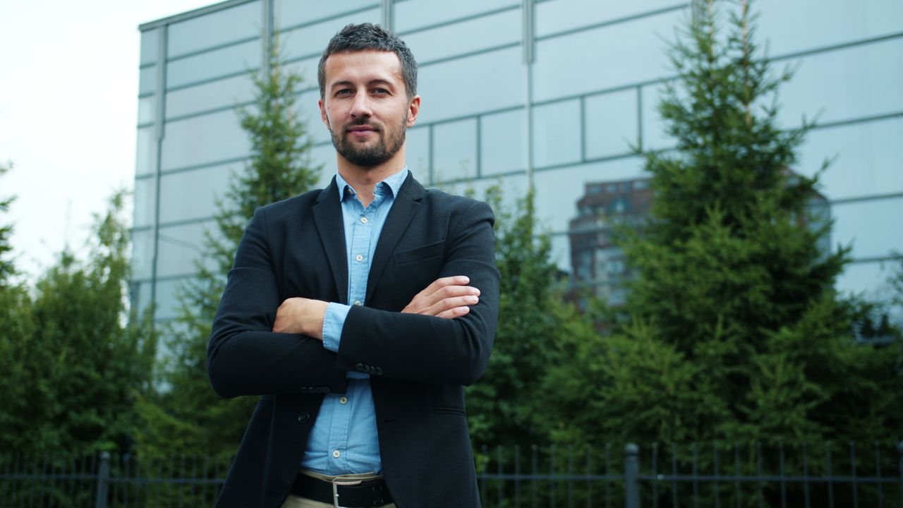 Businessman with arms crossed in front of modern office building, outdoors.