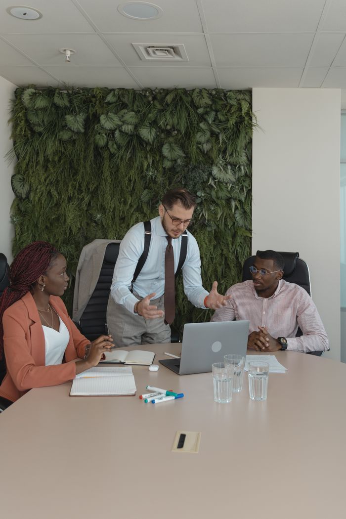 A diverse team discusses ideas in a modern office with a green wall backdrop.